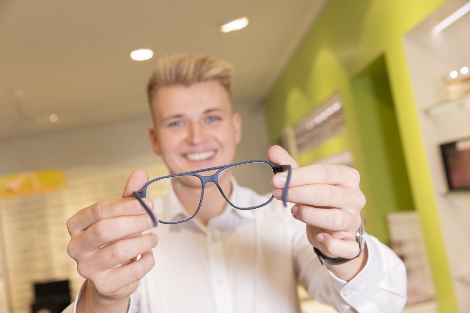 Mitarbeiter im Brillengeschäft mit Brille in der Hand